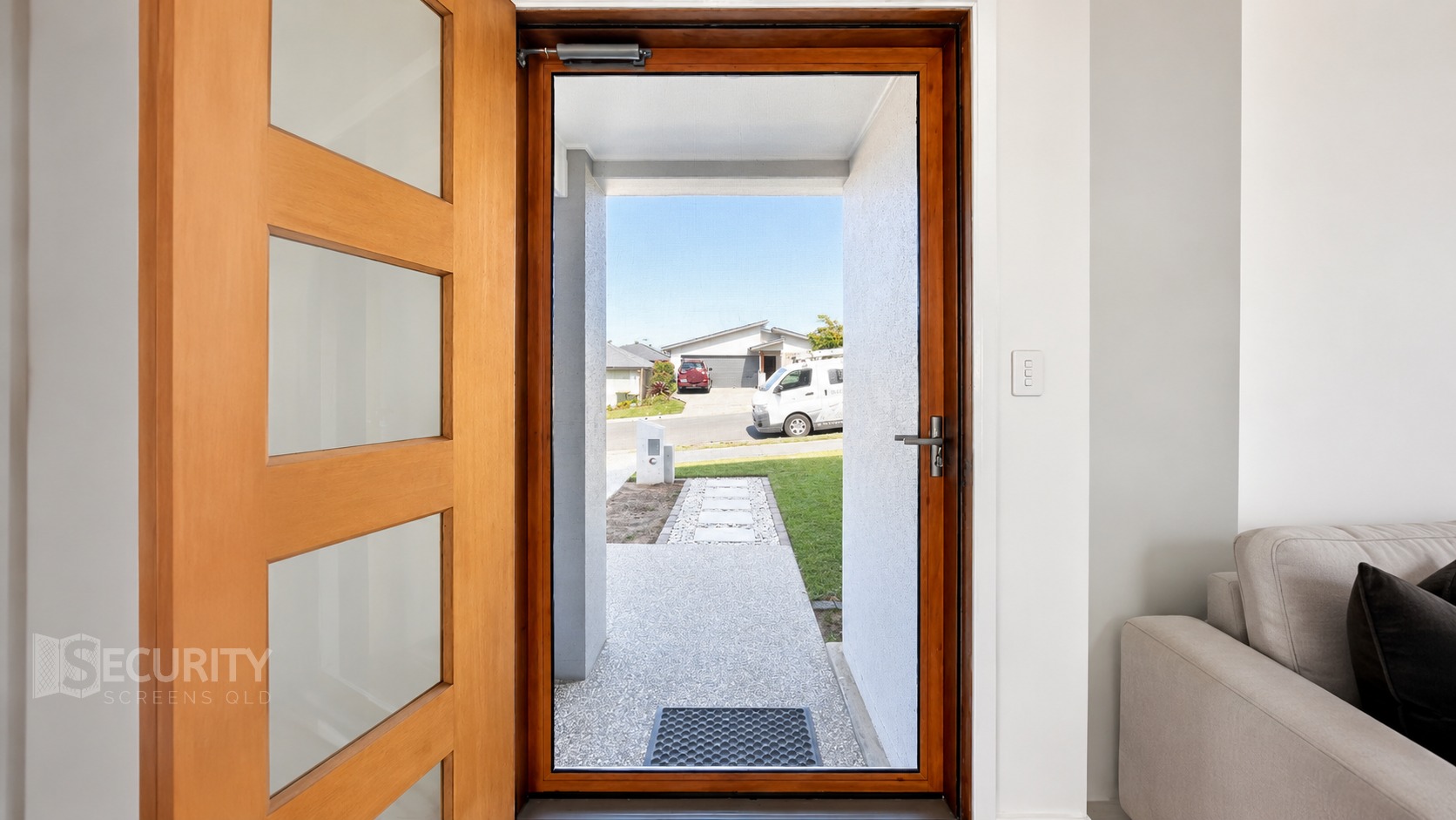 Modern woodgrain finish hinge security screen door installed at residential front entry in Brisbane, featuring frosted glass panels and contemporary design with outdoor pathway visible through open door.