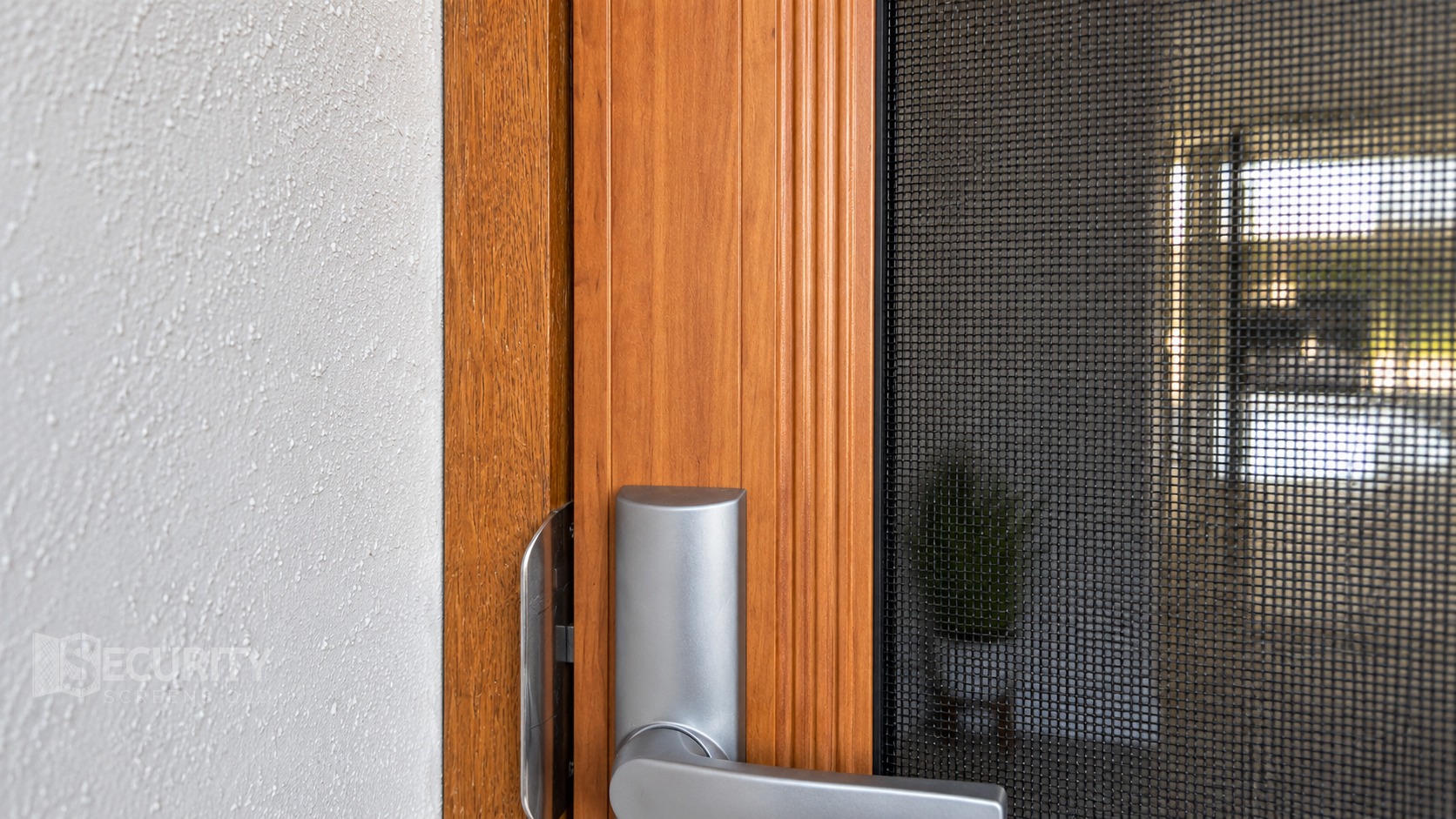 Close-up of a modern stainless steel handle on a woodgrain security screen door with mesh protection, professionally installed in Brisbane. The premium finish complements residential aesthetics while providing security.